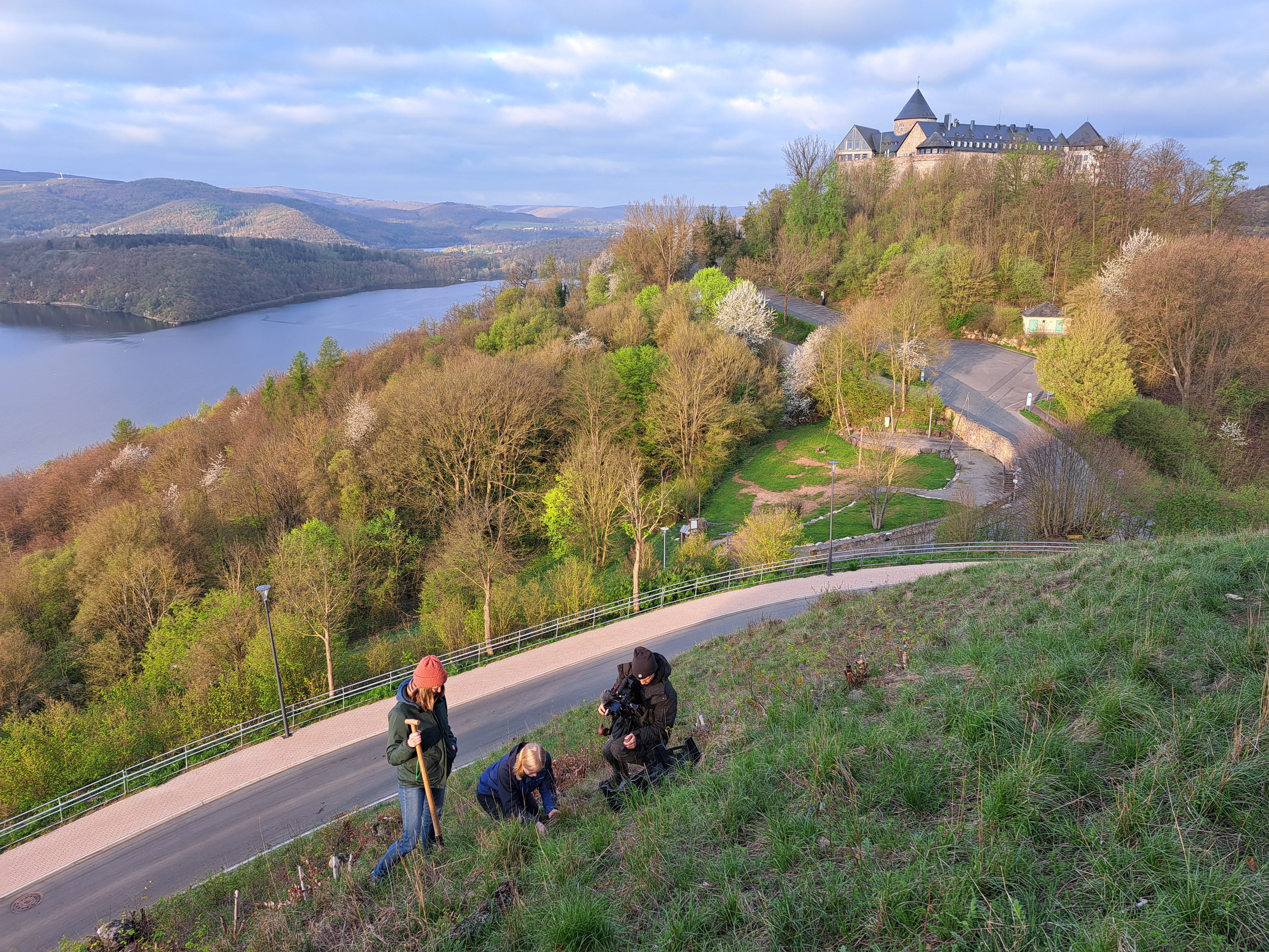 Die beiden Mitarbeiterinnen des Landschaftspflegeverbandes, Laura Lachenicht (links) und Maren Lange, beim Auspflanzen von Kreuz-Enzian mit phantastischem Blick auf den Edersee und Schloss Waldeck. Die Pflanzaktion wurde von Thomas Fabry von Fabrykant für einen Imagefilm des LPV begleitet.